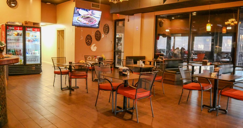 Interior of a restaurant with tables, chairs, a TV, beverage refrigerators, and warm lighting