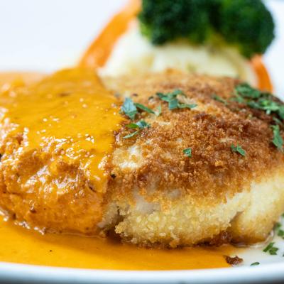 A close up of a dish with breaded chicken topped with creamy orange sauce.