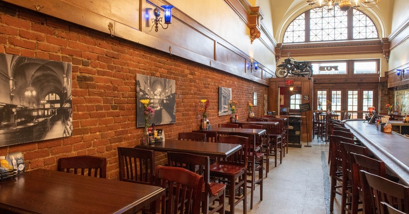 Interior, bar and seating, lined up tables by a brick wall with photo prints