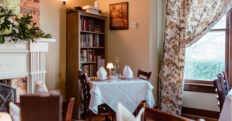 Table for two ready for guests, bookshelf in a corner, window on the right
