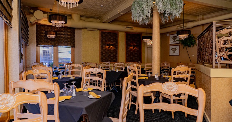 A warm and elegant restaurant interior with tables set for guests under black chandeliers