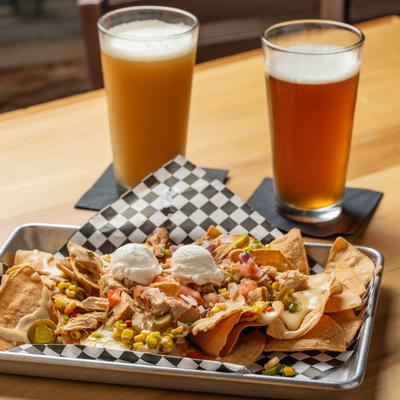 Loaded nachos next to two pints of beer on a wooden table.