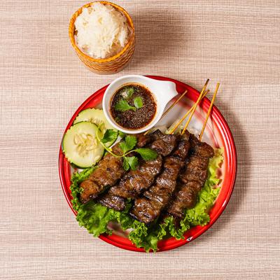 Grilled pork skewers served with sticky rice and chili sauce.