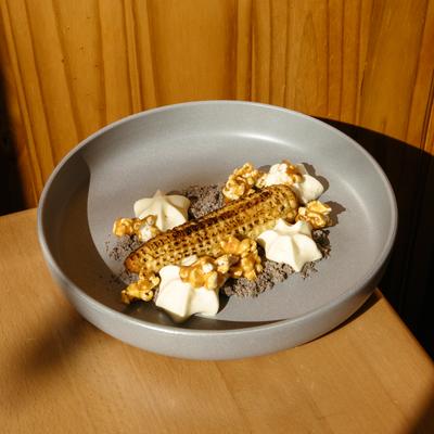 Grilled baby corn with caramel popcorn and cream dollops on a wooden table.