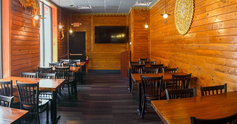 Restaurant interior with wooden walls and tables, black chairs, pendant lights, and a large TV