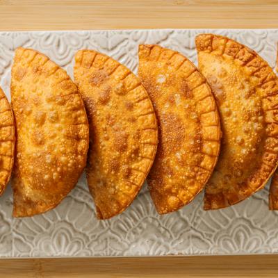 Golden crispy empanadas arranged on a decorative ceramic plate.