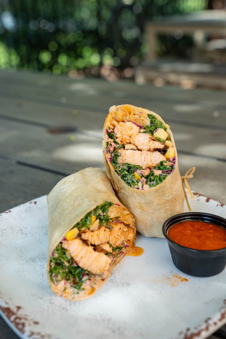 Honey harissa salmon wrap- filled with crunchy kale slaw, charred corn, mango chimichurri, and grilled salmon glazed with honey harissa
