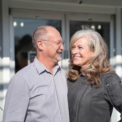 The owners standing in front of the restaurant and smiling at each other.