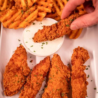 A hand holding a piece of fried chicken and dipping it