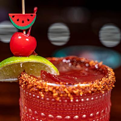 Close up of a red margarita in a glass, with spiced rim, and a lime and cherry skewer.