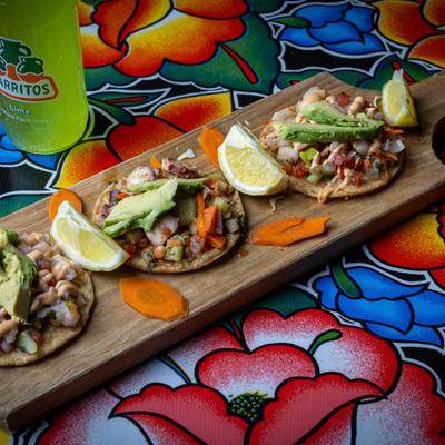 Ceviche street tacos with lime wedges and carrot slices on a long wooden board.