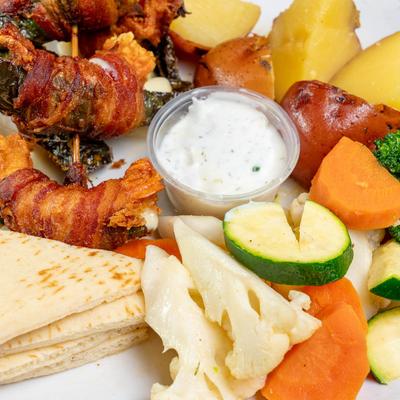 Bacon-wrapped jalapeño poppers with sauce, potatoes, mixed vegetables, and pita bread.