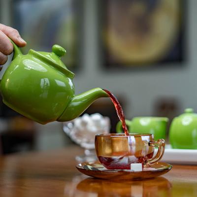 A hand pouring tea from a green teapot into a cup.