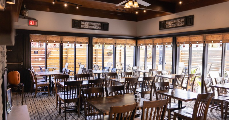 Restaurant interior with wooden tables and chairs, large windows, and a ceiling fan