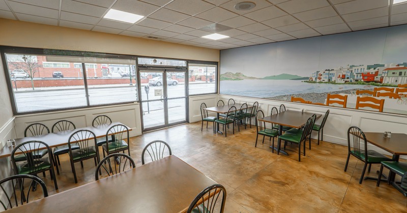 Restaurant dining area with tables and chairs, a large window, and a mural of a coastal scene