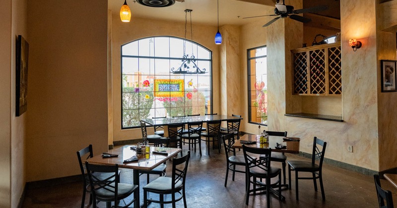 Interior, tables ready for guests, large arched window, wine rack on the right