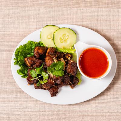 Crispy Thai pork bites with cilantro, lettuce, cucumber slices, and spicy red dipping sauce.