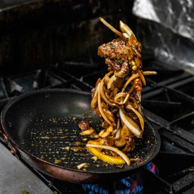 Beef and onion stir-fry being tossed high above a hot skillet.
