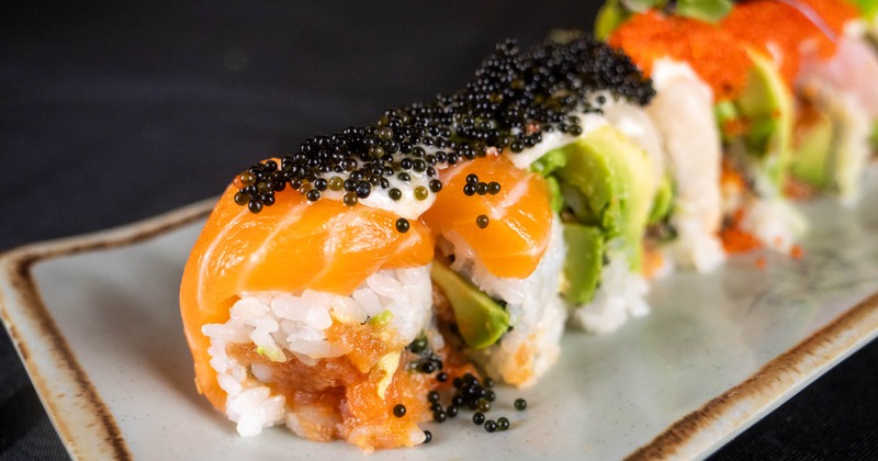 Sushi roll topped with black caviar, salmon slices and avocado