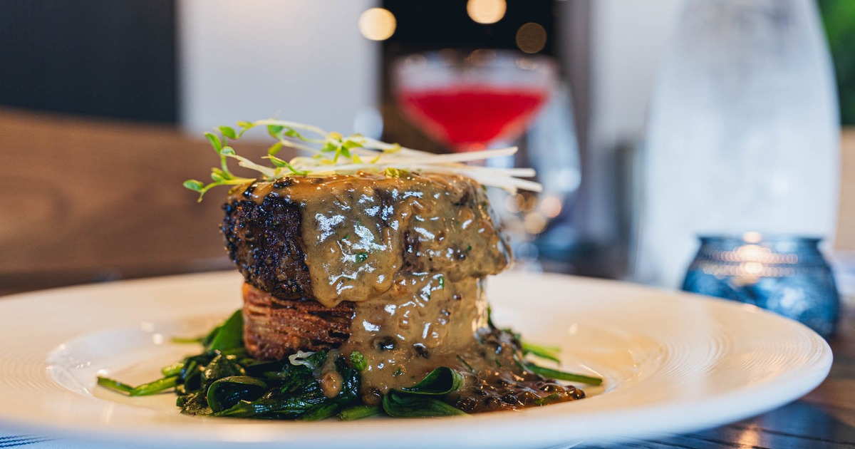 Outdoor dining area with tables and chairs under large beige umbrellas on a sunny day