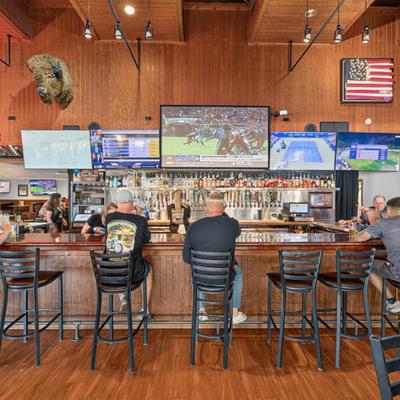 Interior with multiple TV screens mounted behind the wooden bar counter with guests seated.