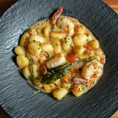 A dish of gnocchi with shrimp in creamy sauce served in a black bowl on a wooden table