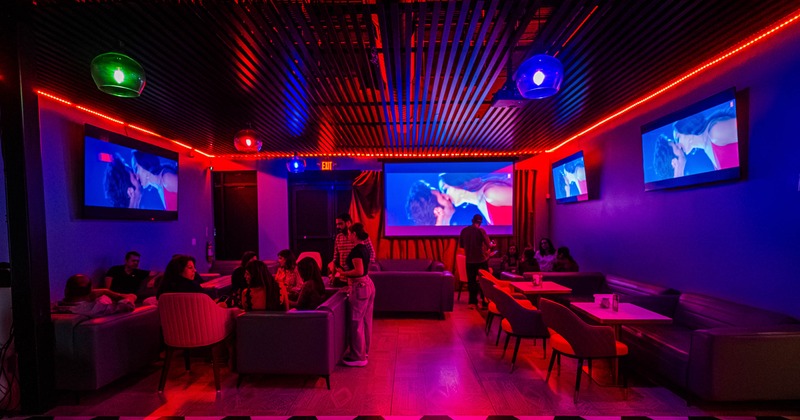 Club lounge with colorful lighting, seating, and multiple screens