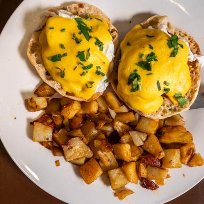 Eggs Benedict topped with hollandaise sauce and herbs, served with home fries.
