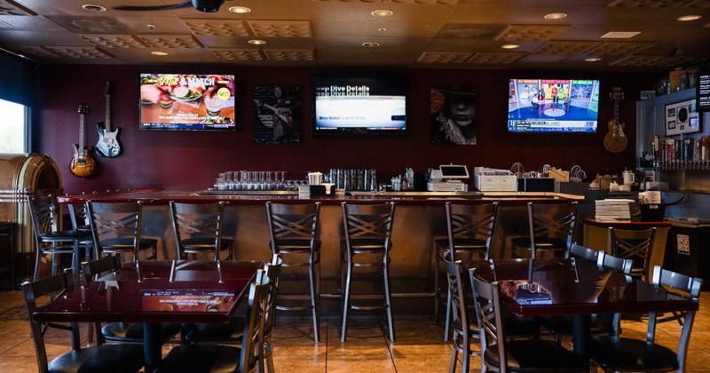 Interior seating area and bar with upholstered stools and TVs above