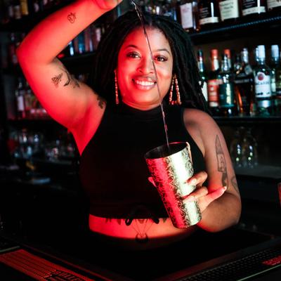 Bar staff smiling, looking at the camera and pouring a drink in shaker.