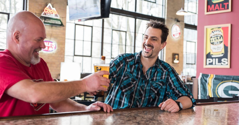 Two men sitting at the bar counter holding drinks, cheers
