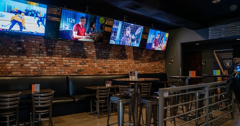 Inside, banquette seating with tables and chairs by a brick wall with TVs