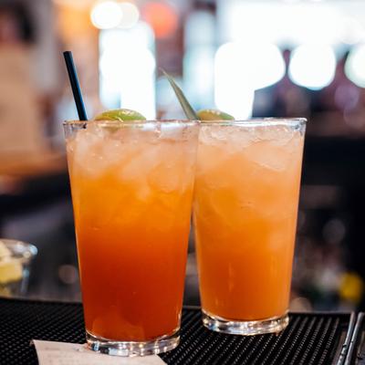 Two orange cocktail drinks on a bar counter mat.