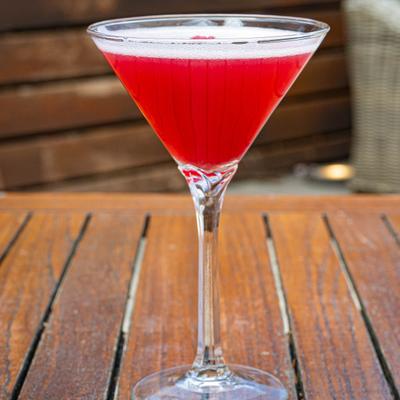 A red cocktail in a martini glass on a wooden table.