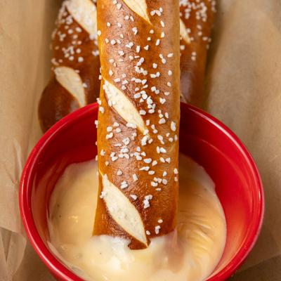 Soft pretzel sticks served with cheese dip in a red bowl.