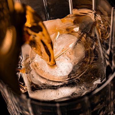 Pouring a golden brown drink over an ice cube in a glass, close up.