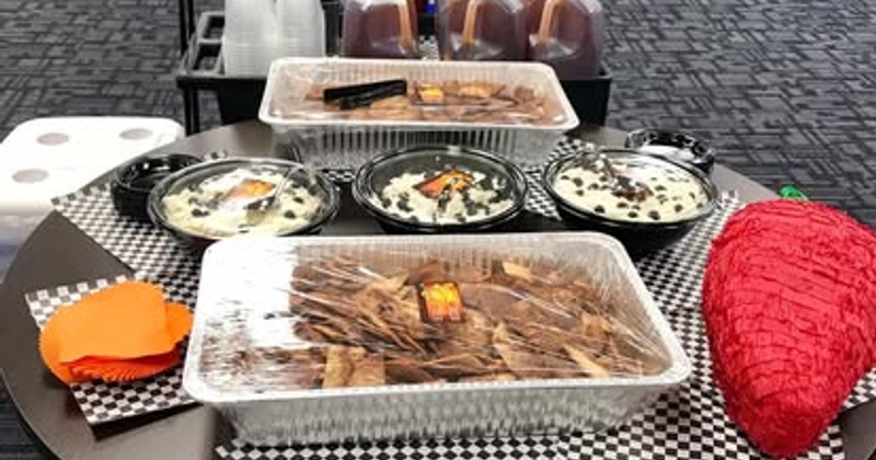 Catering setup with large foil pans of food and a large chili-shaped piñata