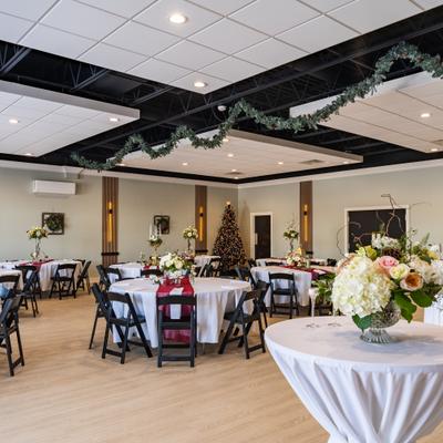 Elegant banquet room featuring round dining tables, floral arrangements, and holiday decorations.