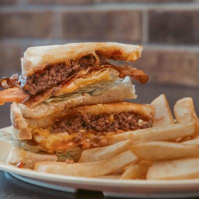 Stacked club sandwich with beef, bacon, lettuce, and tomato, served with fries.