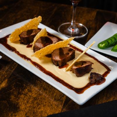 Sliced beef strip steak with sauce and crisps on a rectangular white plate.