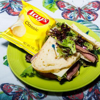 Roast beef sandwich, served on a plate along with the small Lay chips bag.