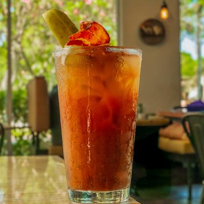 Bloody Mary glass on a table with  blurred outdoor greenery visible through large windows.