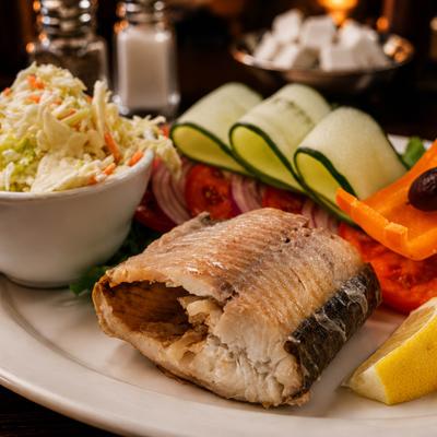 Grilled fish fillet served with coleslaw, fresh vegetables and a lemon wedge.