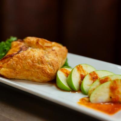 A flaky pastry accompanied by sliced green apples drizzled with sauce.