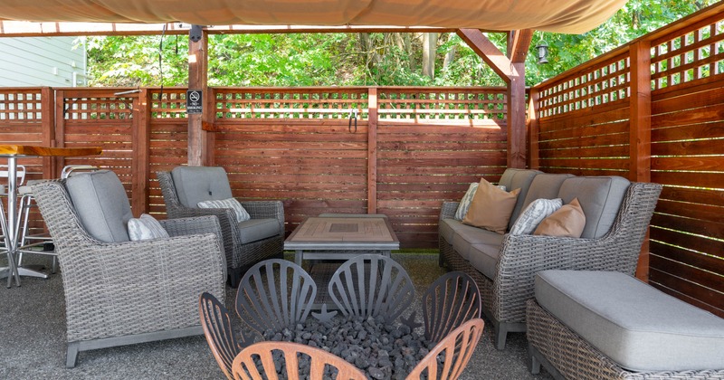 Outdoor seating area with gray wicker furniture, a wooden coffee table, and a shell-shaped fire pit