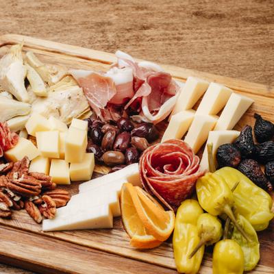 Charcuterie board with cheeses, cured meats, olives, and peppers.