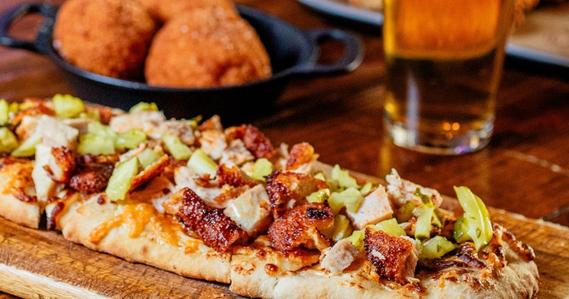 Nashville Chicken Pizza, mac and cheese balls and a glass of beer on a wooden table