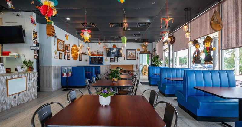 Interior - blue booths, wooden tables, hanging folk-art decorations, large shaded windows.