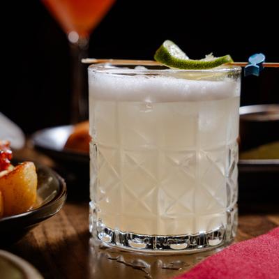 A Margarita cocktail, flanked by food plates, on a wooden table.