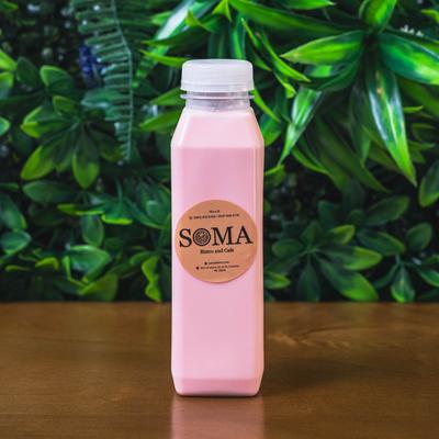 Pink bottled Soma drink on a wooden table with green foliage in the background.